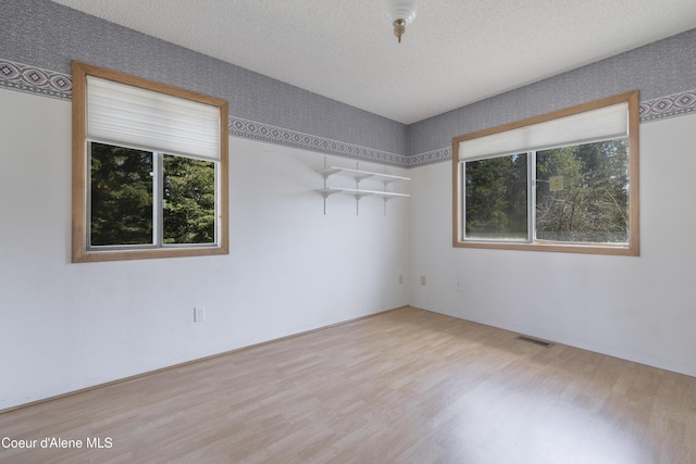 empty room featuring visible vents, wood finished floors, a textured ceiling, and plenty of natural light