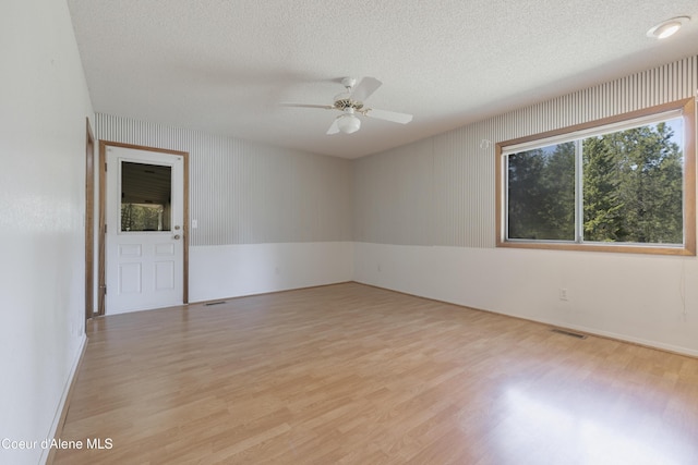 empty room featuring a textured ceiling, ceiling fan, light wood-style flooring, and visible vents