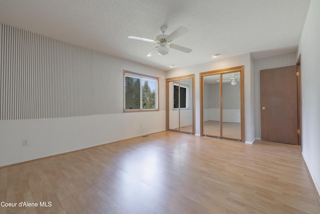 unfurnished bedroom with ceiling fan, light wood-style floors, a textured ceiling, and multiple closets