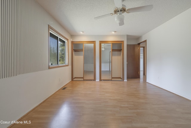 unfurnished bedroom with a textured ceiling, wood finished floors, and multiple closets