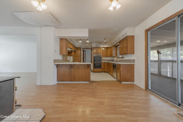 kitchen with brown cabinets, light wood-type flooring, a peninsula, light countertops, and dobule oven black