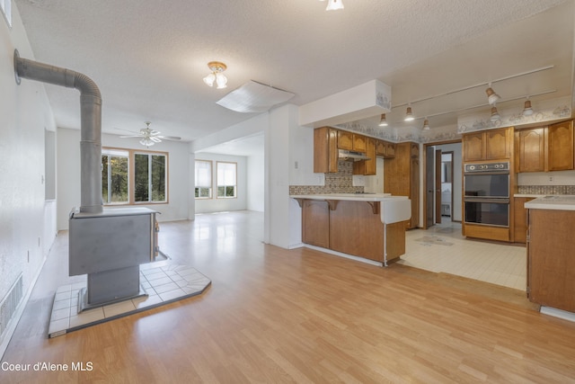 kitchen with a peninsula, light wood-style floors, dobule oven black, a wood stove, and open floor plan