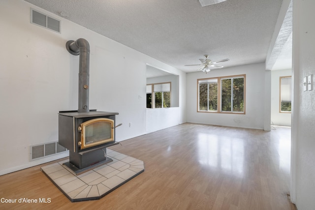unfurnished living room featuring a wood stove, a textured ceiling, and visible vents