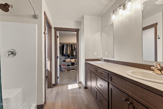 bathroom with walk in shower, a sink, double vanity, wood finished floors, and a spacious closet