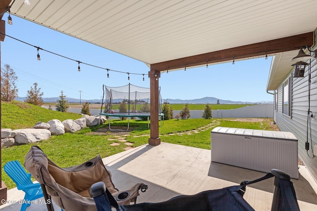 view of patio featuring fence, a mountain view, and a trampoline