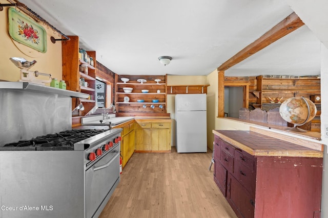 kitchen with high end stove, open shelves, light wood-type flooring, a sink, and freestanding refrigerator