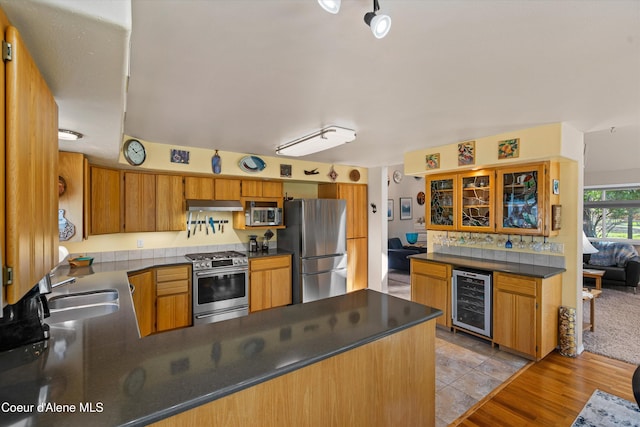 kitchen with a sink, under cabinet range hood, stainless steel appliances, a peninsula, and beverage cooler