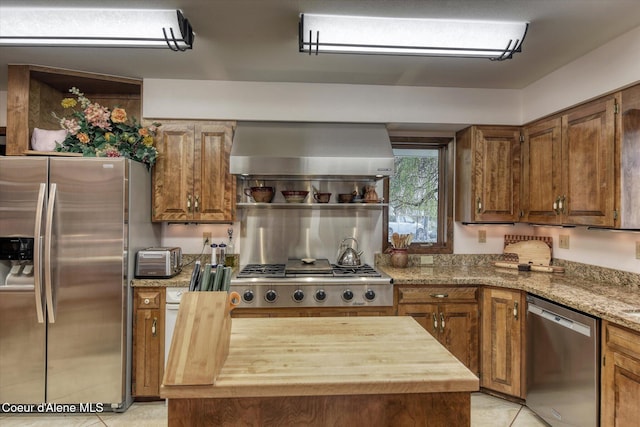 2885 S Folsom Ridge Rd, Coeur Dalene, ID 83814 - kitchen with appliances with stainless steel finishes, wall chimney range hood, light tile patterned flooring, brown cabinetry, and wood counters