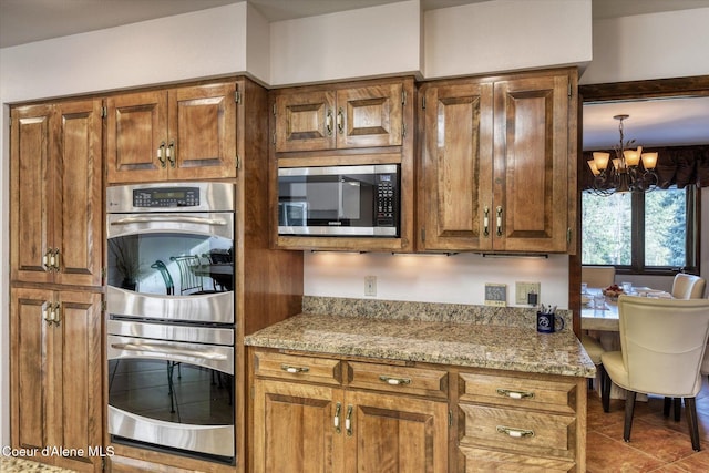 2885 S Folsom Ridge Rd, Coeur Dalene, ID 83814 - kitchen featuring appliances with stainless steel finishes, a chandelier, brown cabinets, light stone countertops, and tile patterned flooring