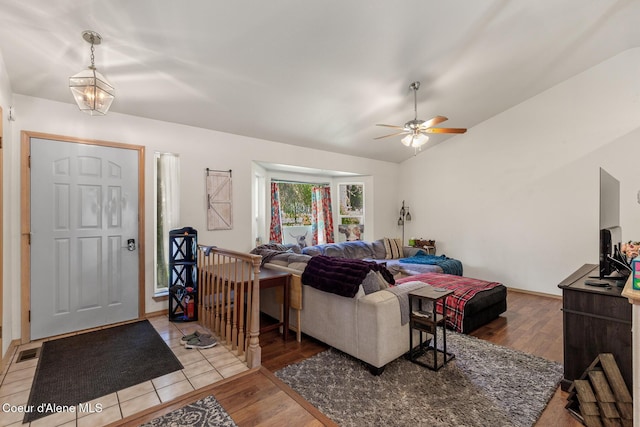 living area with vaulted ceiling, ceiling fan with notable chandelier, light wood-style flooring, and visible vents