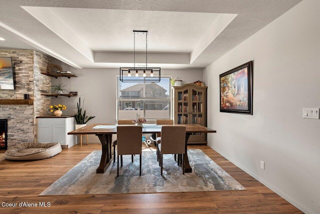 dining area with a fireplace, a raised ceiling, baseboards, a textured ceiling, and wood finished floors