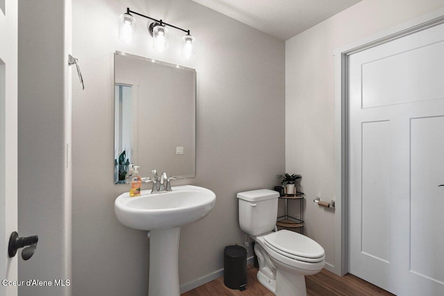 half bathroom featuring wood finished floors, toilet, and baseboards