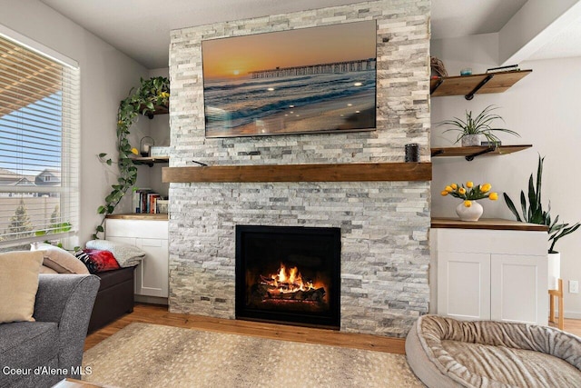 living room with a stone fireplace, wood finished floors, and a healthy amount of sunlight