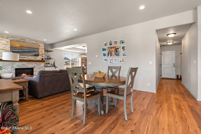 dining room featuring baseboards, recessed lighting, wood finished floors, and a stone fireplace