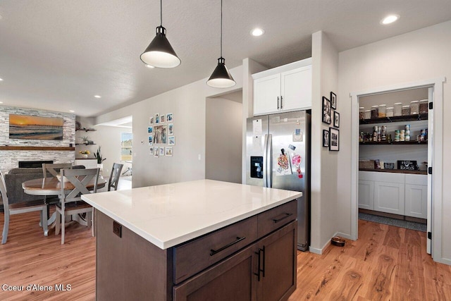 kitchen with decorative light fixtures, light wood-style floors, stainless steel fridge with ice dispenser, white cabinets, and a stone fireplace