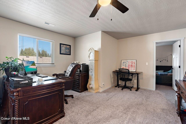 office space with a textured ceiling, light colored carpet, visible vents, baseboards, and a ceiling fan