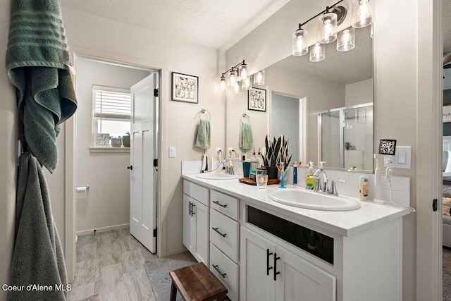 bathroom featuring double vanity, a shower stall, baseboards, and a sink