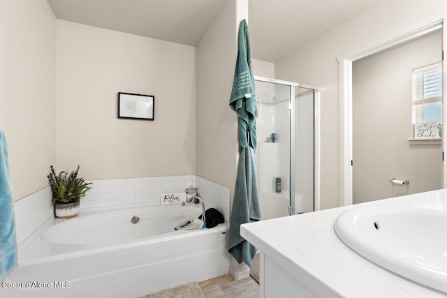 full bath with a stall shower, a textured ceiling, a bath, and vanity