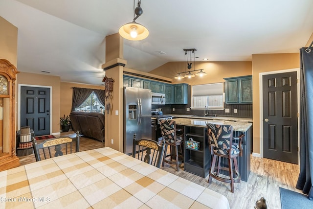 kitchen with a sink, stainless steel appliances, a kitchen bar, decorative light fixtures, and vaulted ceiling