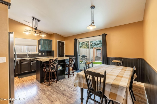 dining area featuring a wainscoted wall, visible vents, lofted ceiling, and light wood-style floors