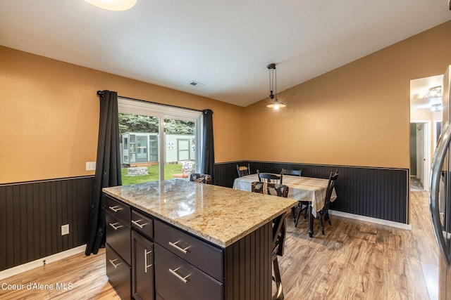 kitchen featuring pendant lighting, light wood-style floors, visible vents, vaulted ceiling, and wainscoting