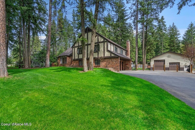 tudor home featuring fence, brick siding, a garage, a front yard, and an outbuilding