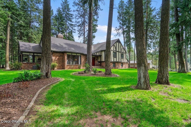 tudor-style house featuring brick siding, a chimney, and a front lawn
