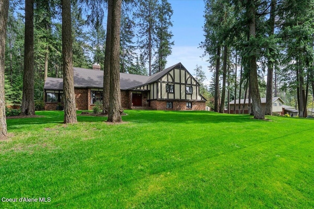 view of front of home with brick siding, a chimney, and a front lawn
