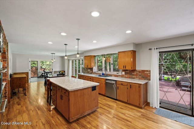 kitchen featuring stainless steel dishwasher, brown cabinetry, light countertops, a sink, and light wood finished floors