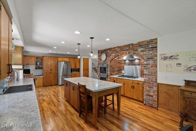 kitchen featuring brown cabinetry, a center island, a sink, stainless steel appliances, and light wood-style flooring