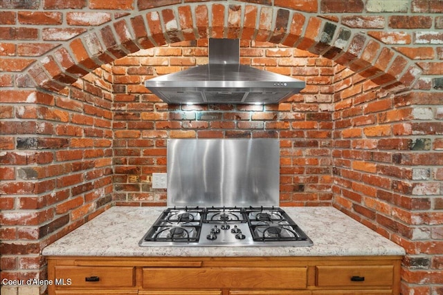 interior details featuring stainless steel gas cooktop, light stone countertops, and extractor fan