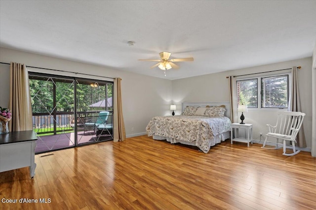 bedroom with baseboards, light wood-style flooring, multiple windows, and access to exterior