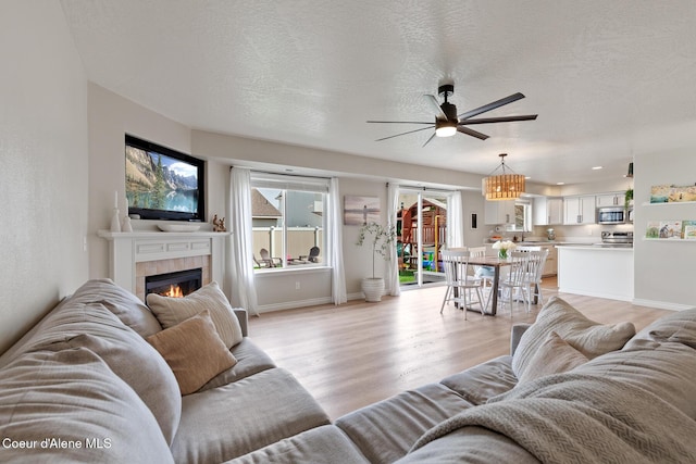 living area featuring a textured ceiling, ceiling fan, light wood-style floors, baseboards, and a tile fireplace