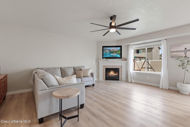 living area featuring a tile fireplace, ceiling fan, baseboards, and light wood-type flooring