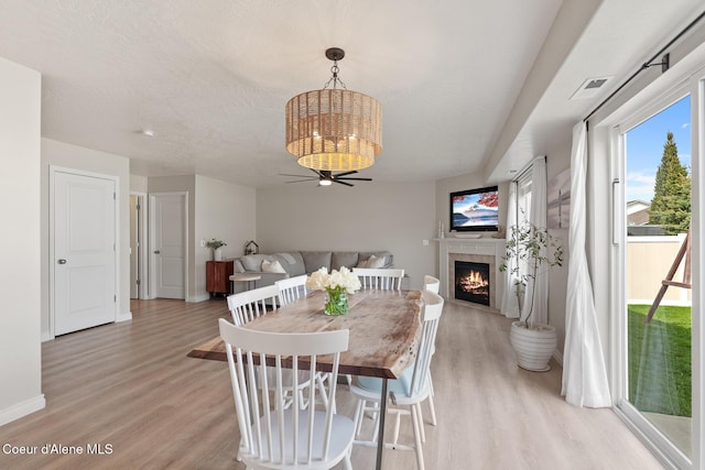 dining area featuring a fireplace, baseboards, light wood finished floors, and a notable chandelier