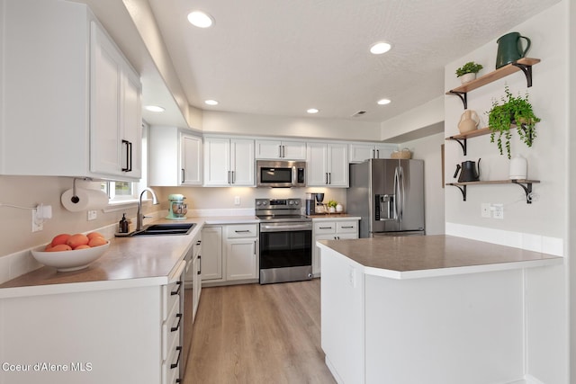 kitchen featuring open shelves, light wood-style floors, appliances with stainless steel finishes, a sink, and white cabinetry