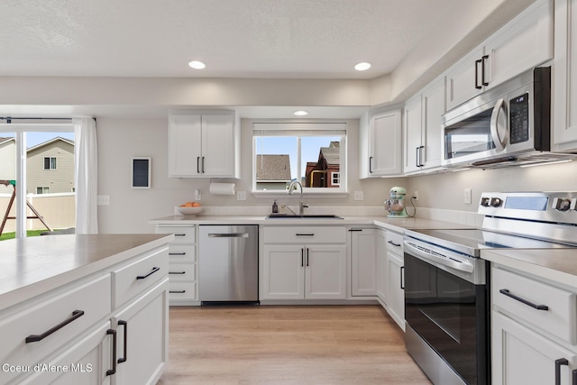 kitchen featuring light wood-style flooring, white cabinets, a sink, stainless steel appliances, and recessed lighting