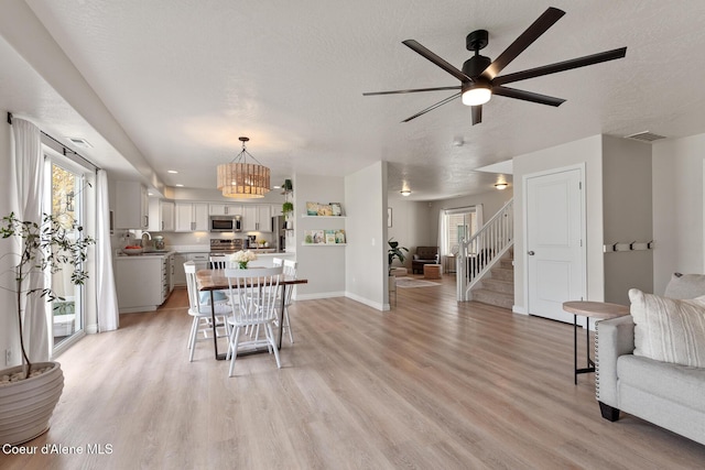 living room with stairs, baseboards, ceiling fan with notable chandelier, and light wood-style floors