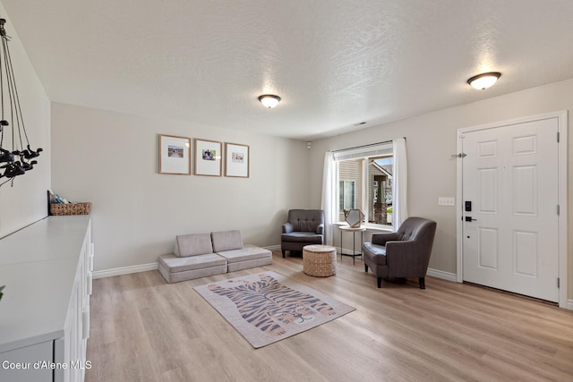 living area with a textured ceiling, baseboards, and light wood-style floors