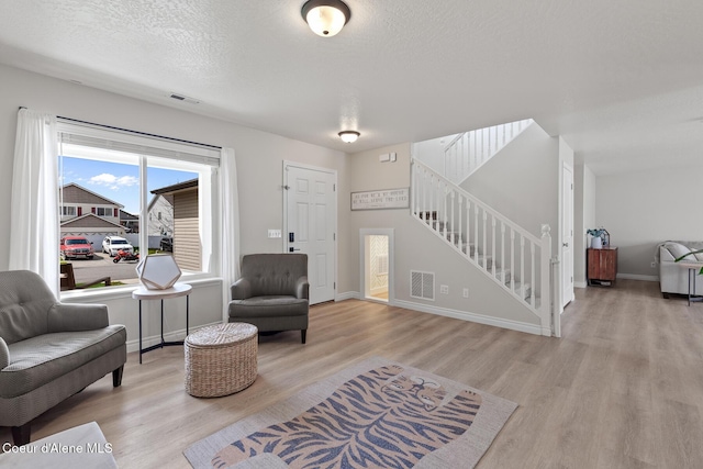 living area featuring stairway, visible vents, baseboards, a textured ceiling, and wood finished floors