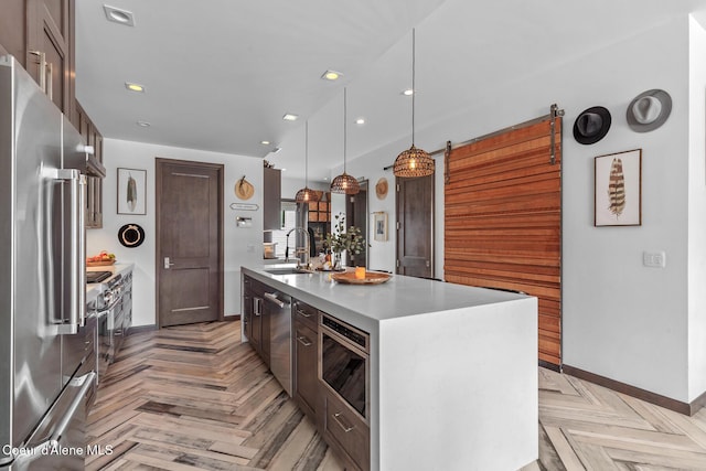 kitchen with a kitchen island with sink, appliances with stainless steel finishes, light countertops, a sink, and baseboards