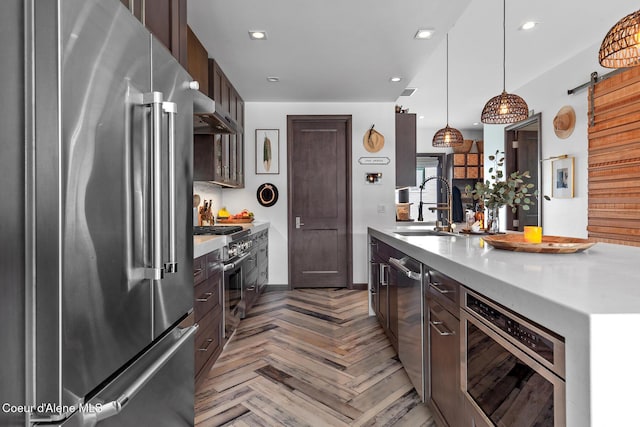 kitchen with high end appliances, light countertops, dark brown cabinets, a sink, and ventilation hood