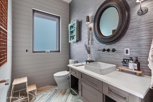 bathroom featuring toilet, wooden walls, and vanity