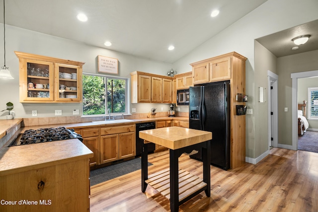 kitchen with a sink, light wood-style floors, light countertops, glass insert cabinets, and black appliances