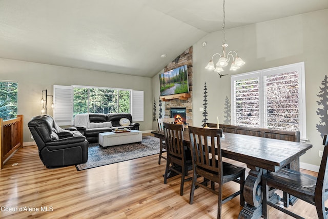dining space with an inviting chandelier, light wood-style flooring, high vaulted ceiling, and a stone fireplace