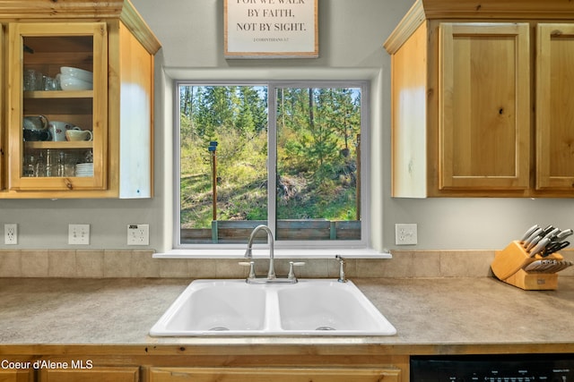 kitchen featuring a sink, light countertops, a healthy amount of sunlight, glass insert cabinets, and dishwashing machine