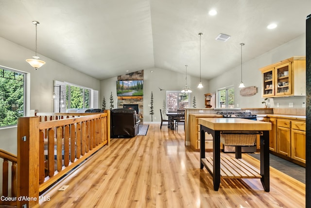 kitchen with a peninsula, lofted ceiling, glass insert cabinets, light countertops, and light wood finished floors