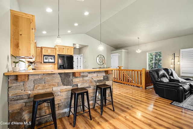 interior space featuring a breakfast bar area, vaulted ceiling, stainless steel microwave, black refrigerator with ice dispenser, and light wood-style floors
