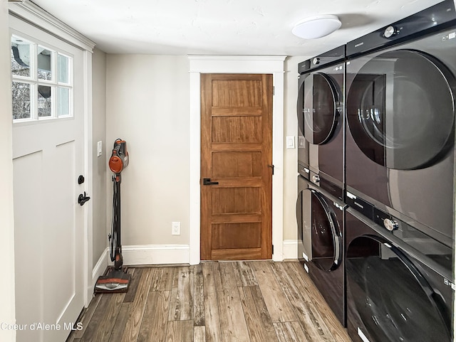 laundry room with wood finished floors, stacked washer / dryer, and baseboards