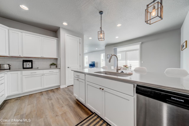 kitchen with hanging light fixtures, light wood-style flooring, dishwasher, a sink, and white cabinetry
